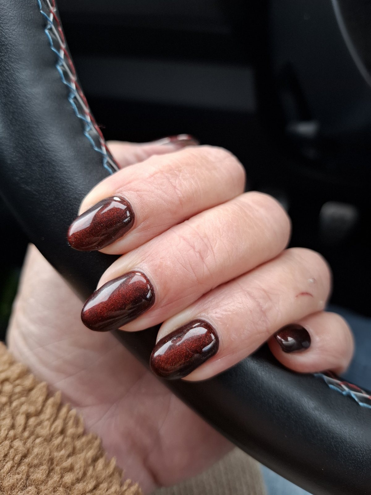 Donkerrode glanzende nagels van een klant, de hand op een stuur